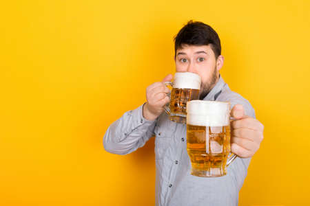 man drinks beer and offers the viewer a glass of beer, image on a yellow backgroundの写真素材