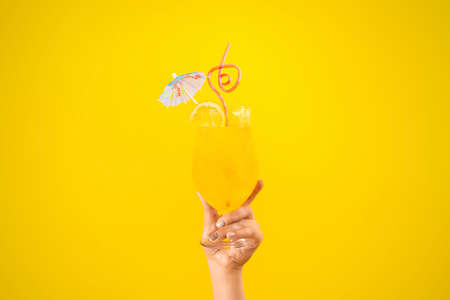 Orange fresh summer cocktail in female hand on a yellow background, concept drink for coolingの写真素材