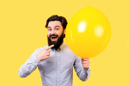 bearded smiling man pointing away on a yellow balloon with a smileの写真素材