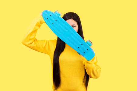 studio portrait of a girl covering her face with a skateboard, image on a yellow background, the...