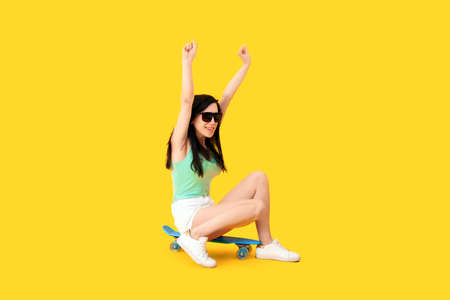 beautiful girl in sunglasses, sitting on a skateboard, image on yellow background, concept positive...