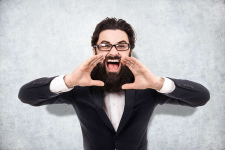 businessman shouting and holding hands near the mouth, image on the background a concrete wall, concept of call to actionの写真素材