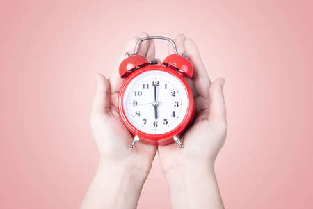 red alarm clock in hands, on pink background, concept time to wake up