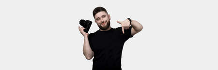 cheerful bearded photographer holding a camera and pointing down, isolated on white background, panoramic imageの写真素材