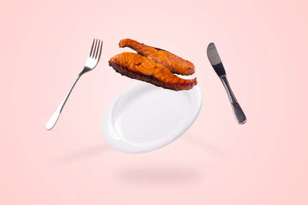grilled salmon fish falling on the levitating plate, fork and knife. conceptual food backgroundの写真素材
