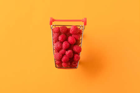 ripe raspberries in shopping cart on orange background, concept buying sweet berries, flat lay.