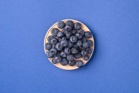 Ripe blueberries in the wooden bowl. Top view, summer berries on a blue backgroundの写真素材