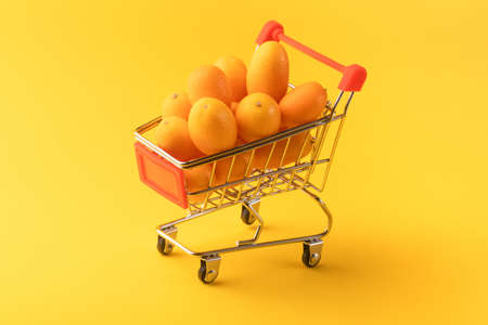 Cumquat or kumquat in a shopping cart on yellow background, fruit shopping concept