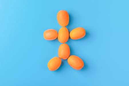 Man figure made of Kumquat fruits on blue background