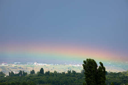 Natural rainbow over green trees, summer city landscape