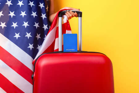 Passport with USA flag on red suitcase. American visa, work and travel concept, suitcase with hand over yellow backgroundの写真素材