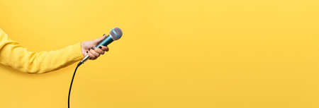 hand holding microphone over yellow background, panoramic mock up imageの写真素材