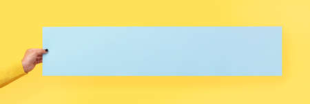 Mockup empty blank blue postcard holds the girl in her hand over yellow background, panoramic imageの写真素材