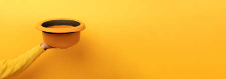 fashionable felt hat in hand over yellow background, panoramic image