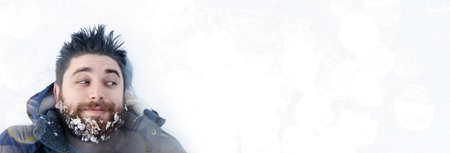 bearded, positive man in the snow  looking at banner with place for text, concept space for your advertisement, panoramic image, seasonal winter advertisingの写真素材