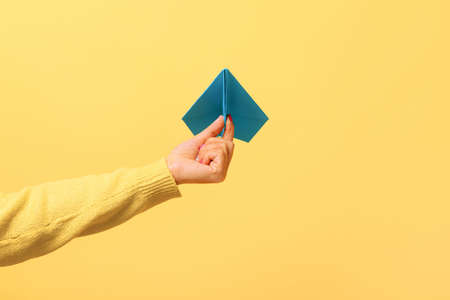 Woman hand holding blue paper airplane over yellow background, freedom concept.の写真素材