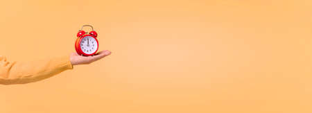 red clock with alarm on hand over orange background, wake up concept in the morning, panoramic mock...