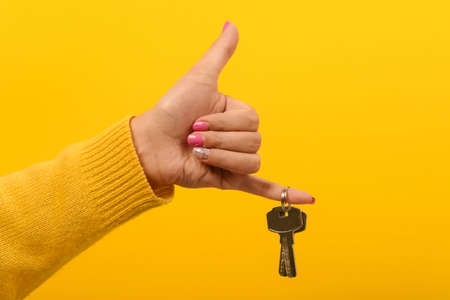 female hand holding house keys and showing thumb up, over yellow background