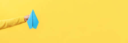 hand holding paper plane over yellow background, panoramic mock up image
