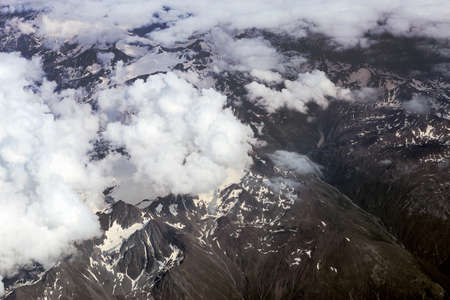 Alps and clouds from the plane. Earth through the porthole. Aerial view, concept of flight trip