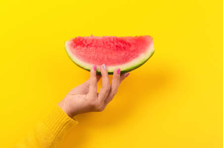 hand holds watermelon slice over yellow background.  Summertime concept.の写真素材