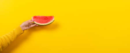 hand holds watermelon slice over yellow background. Summertime concept. Panoramic image with space...