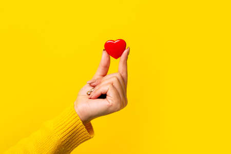 Hand holding a red heart over yellow background, heart health, and donation conceptsの写真素材