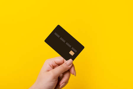 Female hand holding credit card on yellow backgroundの写真素材
