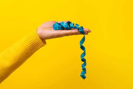 measuring tape on hand over yellow background, diet conceptの写真素材