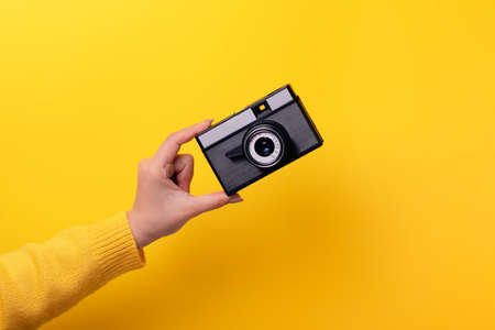 old camera in hand over yellow backgroundの写真素材