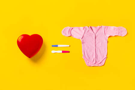 Love is equal to procreation. Red heart, two pregnancy tests in the form of equal and baby suit on a...