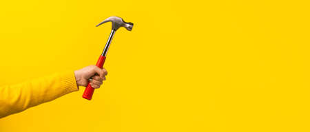 Female hand holding hammer on yellow background, panoramic mock-upの写真素材