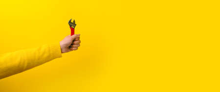 wrench in female hand over yellow background, repair tool, panoramic mock-up with space for textの写真素材