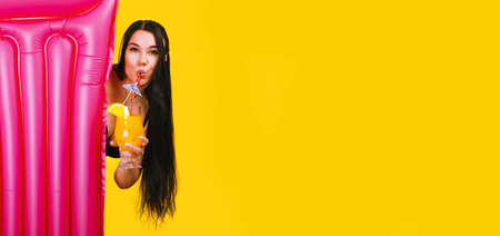 girl with cocktail and swimming mattress over yellow background, summer holiday concept, panoramic...
