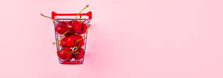 Creative top view of ripe cherries in a shopping cart on pink  background in minimal style. Concept of supermarket or fruit market shopping.の写真素材
