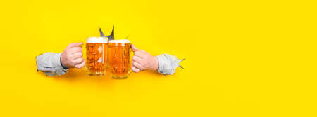 two glasses of beer in the hands,clink glasses on a yellow background