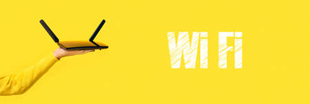 black wifi router on hand and wifi inscription over yellow background, panoramic image