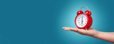 red clock with alarm on hand over blue background, wake up concept in the morningの写真素材