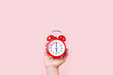 red alarm clock in hand, on pink background, concept time to get upの写真素材