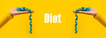 measuring tape on hand over yellow background,  panoramic image with diet inscriptionの写真素材