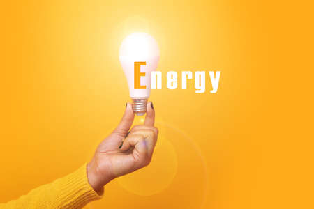 hand holding light bulb with inscription energy, illuminated light bulb, image over yellow backgroundの写真素材