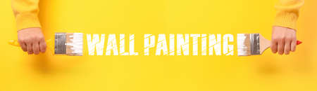 Paint brush in hand over yellow background, wall painting concept, panoramic image