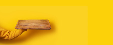 Hand holding wooden board over yellow background, perspective view, panoramic imageの写真素材