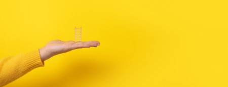 hand holding a ladder over yellow background, education and success conceptの写真素材