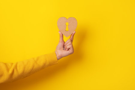 wooden heart with keyhole in hand over yellow backgroundの写真素材