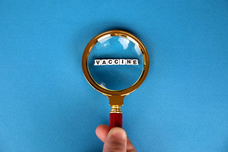 magnifier with vaccine inscription on blue background, vaccine search conceptの写真素材