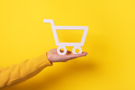 Trolley on hand over yellow background, buying online conceptの写真素材