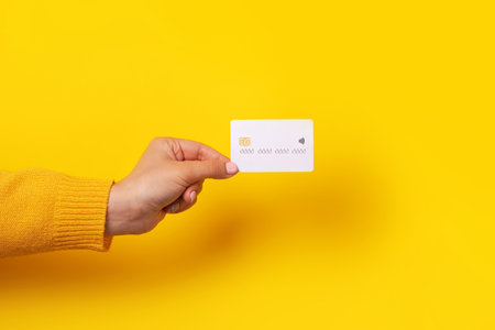 Hand holding blank white credit card mockup, card with electronic chip over yellow backgroundの写真素材