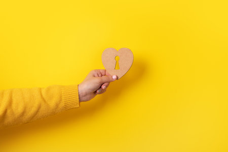 wooden heart with keyhole in hand over yellow backgroundの写真素材