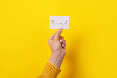 white credit card in female hand, card with electronic chip over yellow backgroundの写真素材